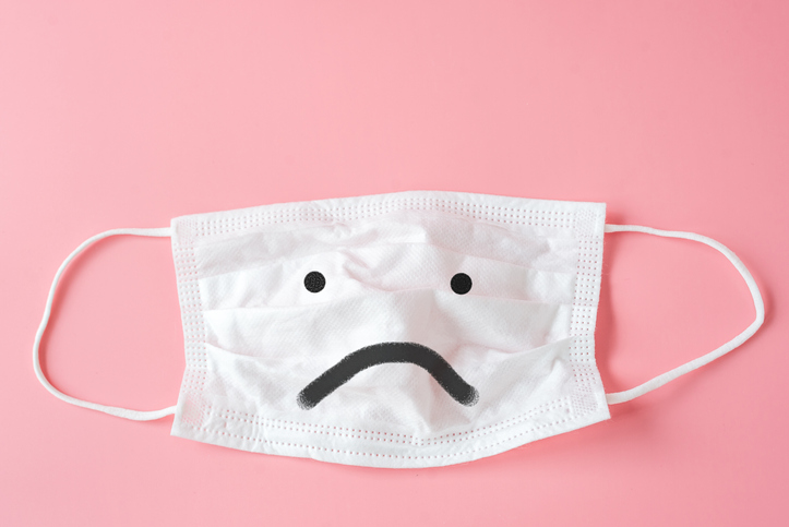 Unhappy face on Protective white face mask on pink background.